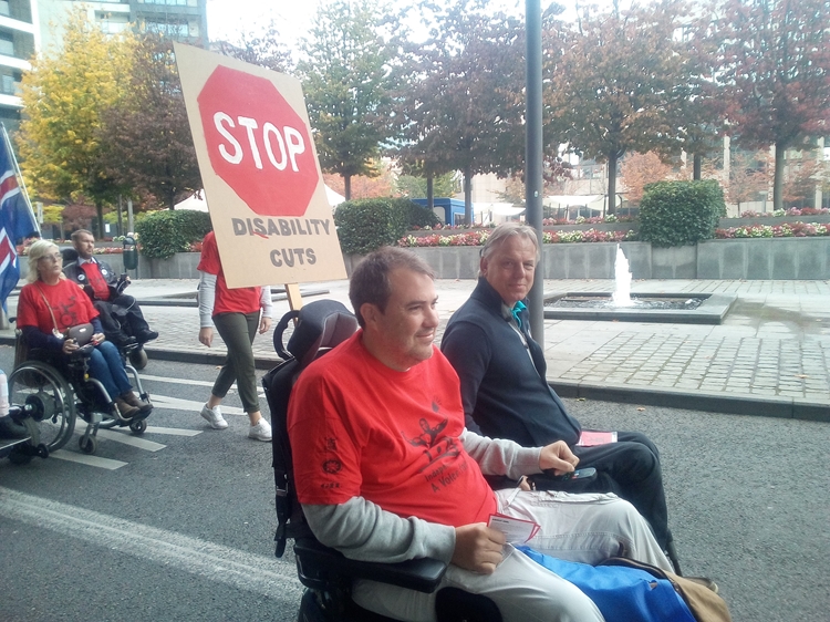 man in rolstoel met bord: stop disability cuts